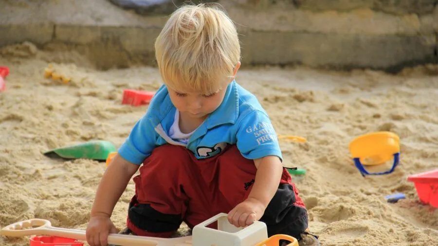 Young child playing and digging in sandbox during outdoor playtime in backyard