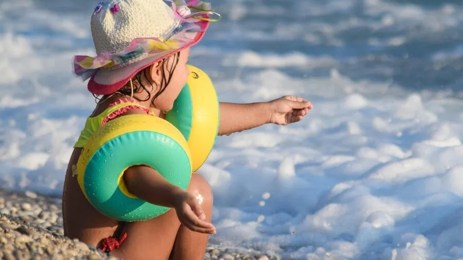 Young child playing in ocean waves at sunny beach with UV protection considerations