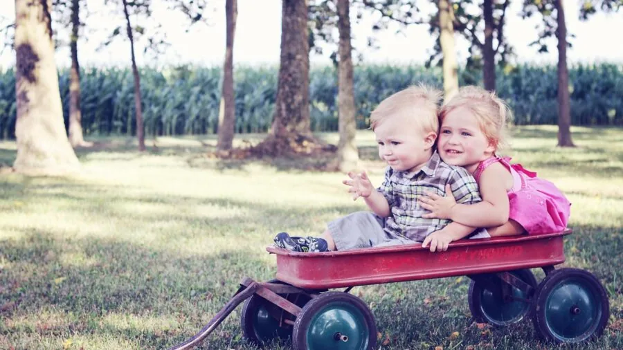 Young child pulling wagon across grassy outdoor surface exploring natural terrain