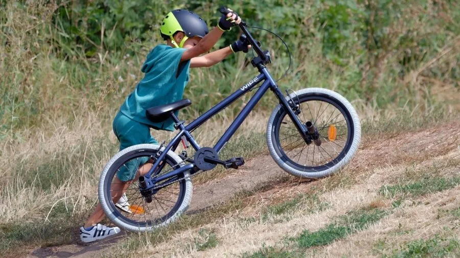 Young child riding a lightweight bike on a forest trail, demonstrating proper cycling form and balance