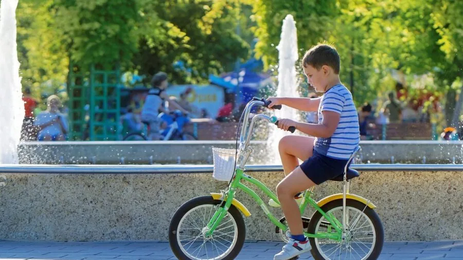 Young child riding bicycle outdoors in bright sunlight wearing protective gear