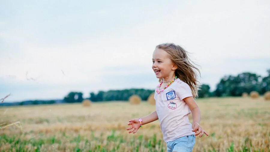Young child running barefoot outdoors on grass during summer, enjoying active play in warm weather
