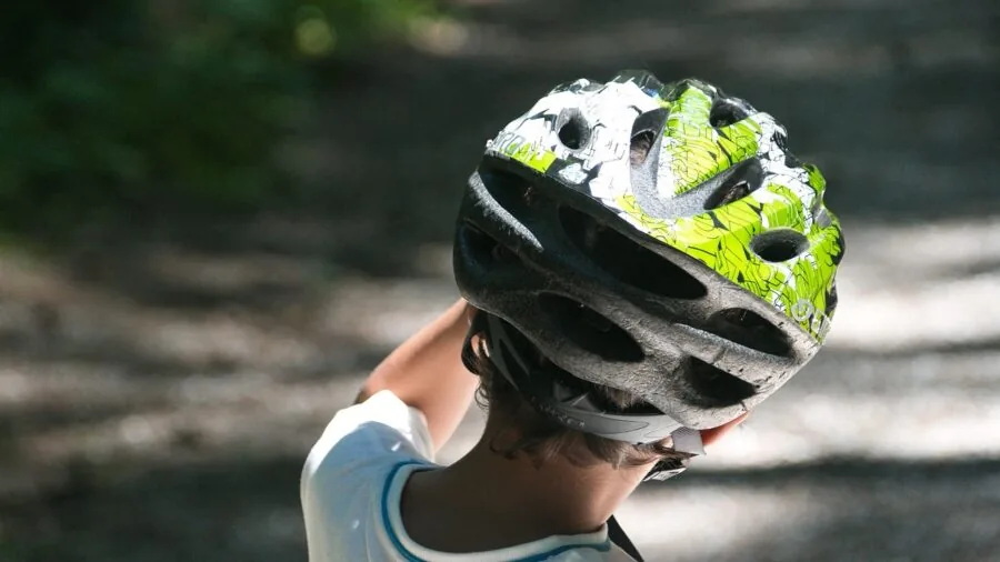 Young child selecting a colorful bike helmet while parent watches, emphasizing active participation in safety gear selection