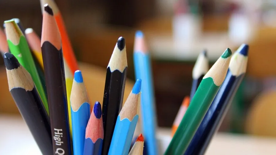 Young child sitting at table drawing with colorful crayons on paper, focused on creative artwork