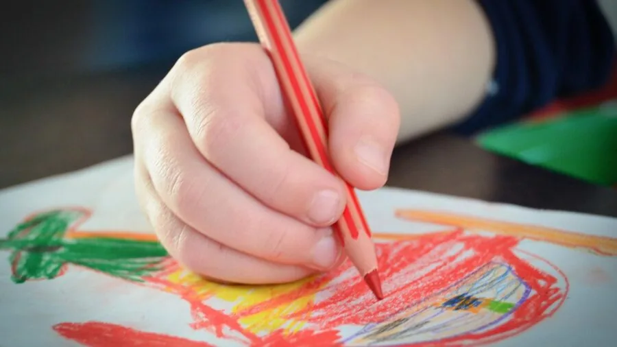 Young child washing colorful paint or crayon residue from hands at bathroom sink