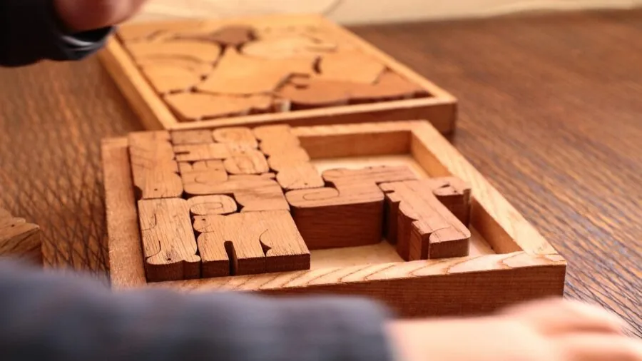 Young child's hands assembling wooden puzzle pieces on a table, focusing on natural wood texture and quality craftsmanship