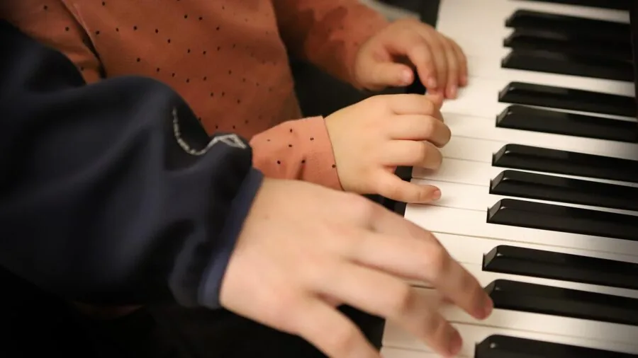 Young child's hands reaching toward piano keyboard keys during music lesson