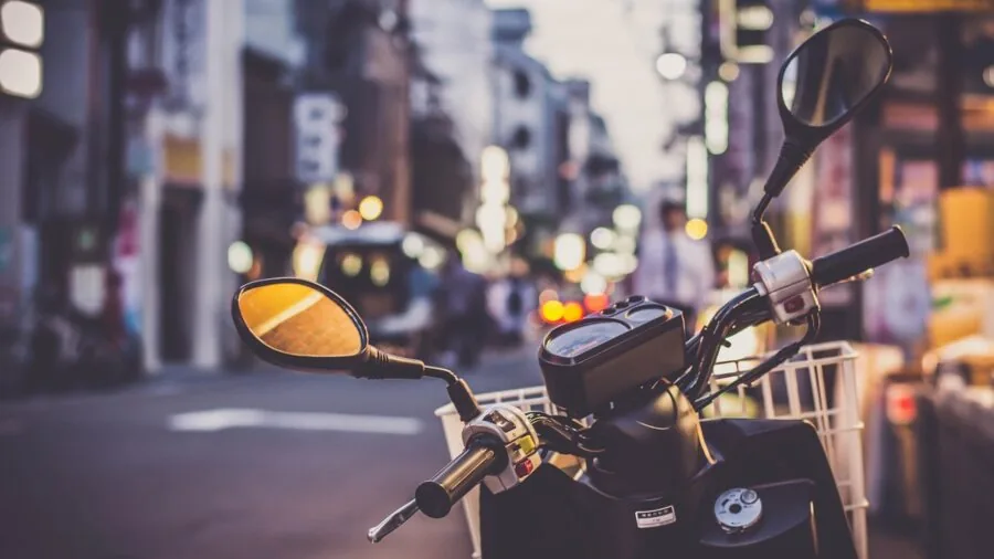 Young commuter holding a kick scooter while walking down a city street with apartment buildings in background