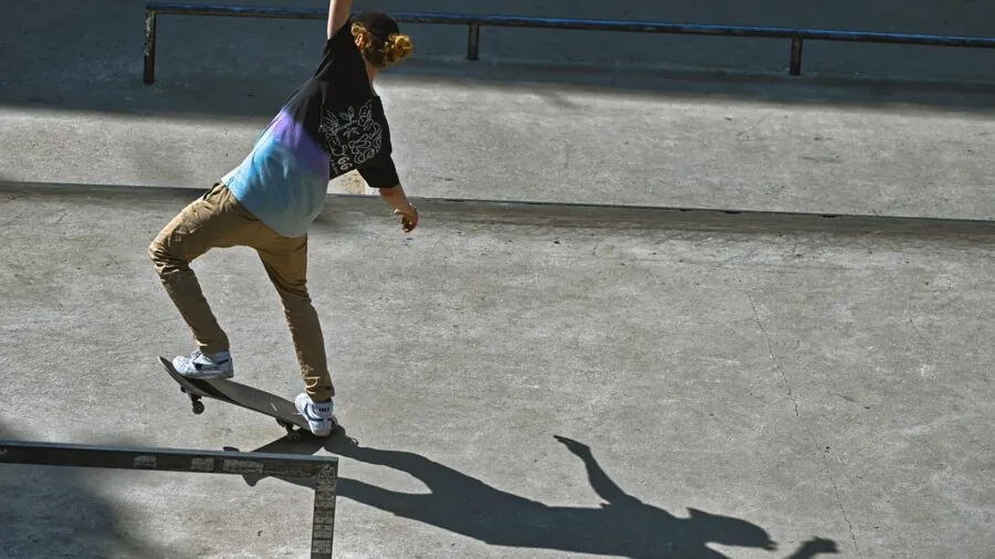 Young skateboarder performing a flip trick on a narrow skateboard in an outdoor skate park setting