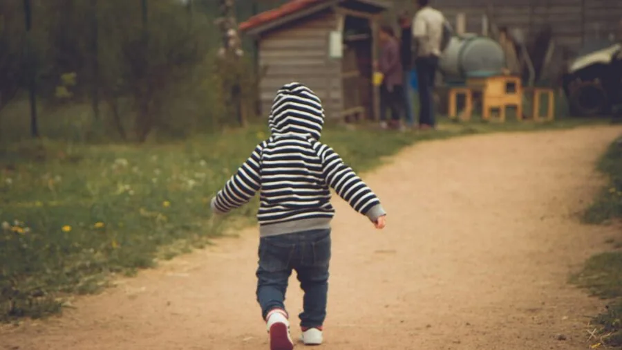 Young toddler taking first steps on grass while parent supervises nearby